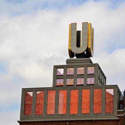 Das beleuchtete goldene U auf dem Dach des Dortmunder U-Turms vor bewölktem Himmel