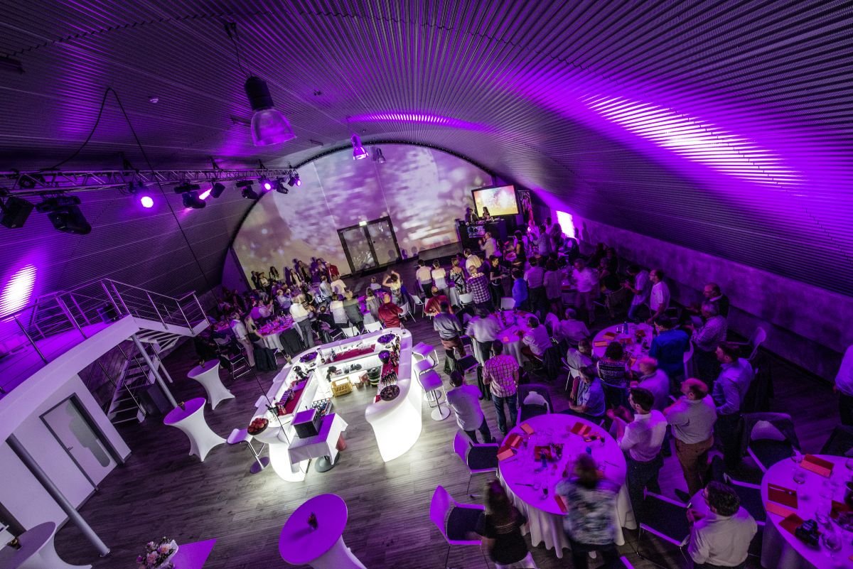 Gesamtansicht einer Hochzeitsfeier mit Gästen und Lichtkonzept in der Hochzeitslocation E210 Eventhangar in Rheinmünster