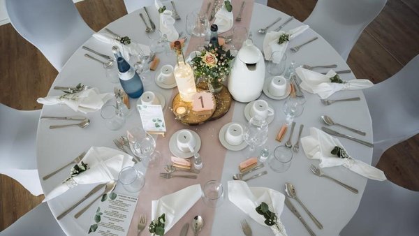 Gedeckter runder Hochzeitstisch im Eventhaus Boger – elegante Tischdekoration mit weißen Hussen, floraler Mitte und fein arrangiertem Besteck.