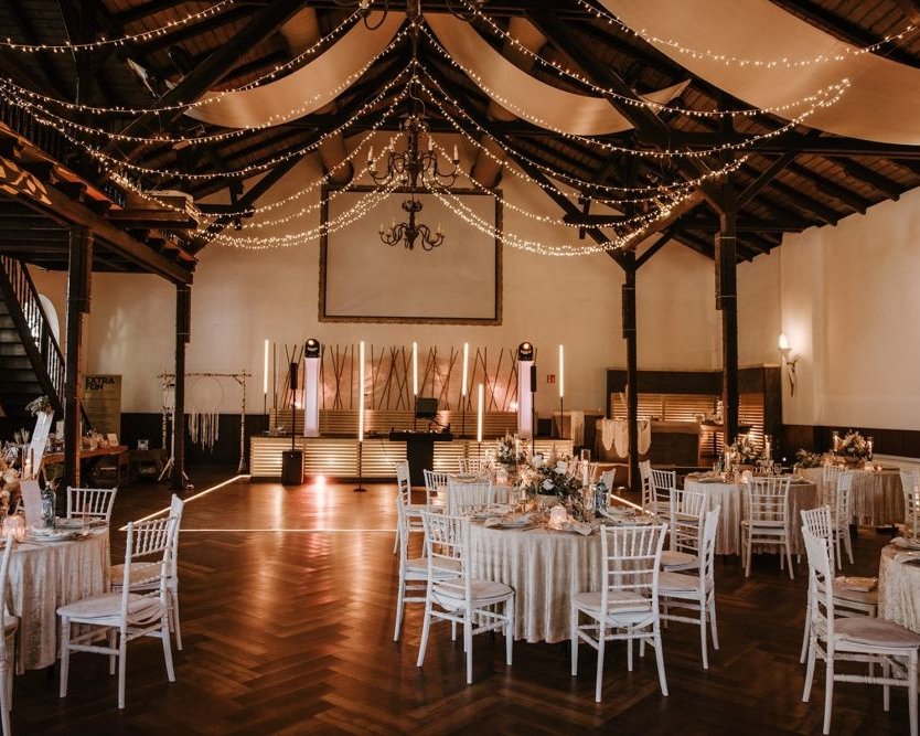 Hochzeitssaal der Hochzeitslocation Extrafein-Witten mit rustikalem Dachgebälk und festlich gedeckten Tischen