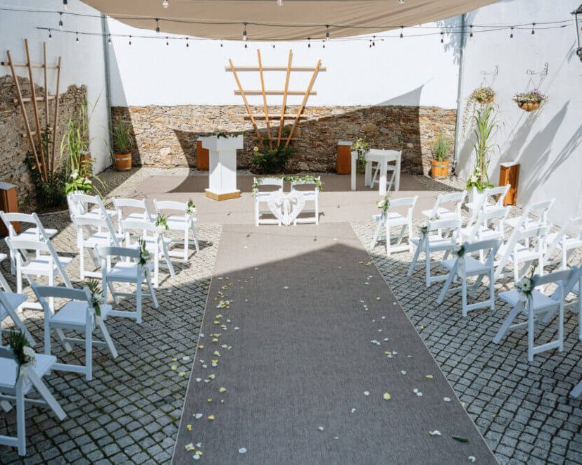 Festlich dekorierte freie Trauung im Innenhof von Schloss Wildeck bei Chemnitz mit weißen Stühlen und Traubogen