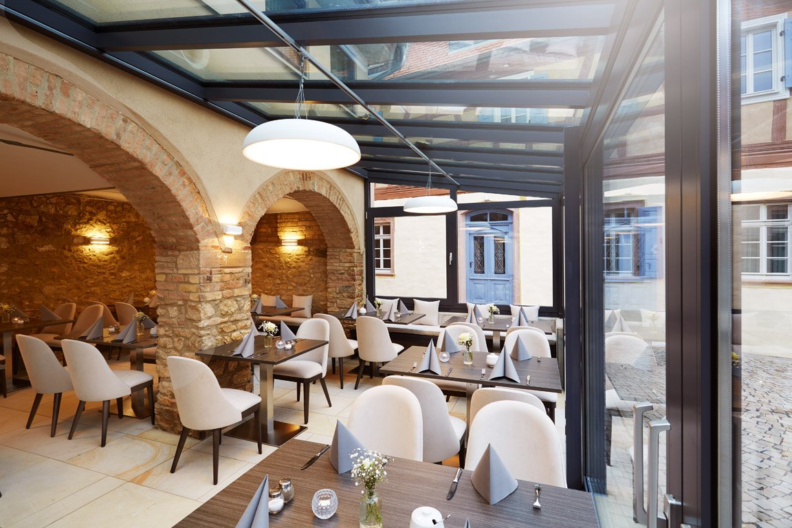 Moderner Gastraum „Remise“ der Hochzeitslocation GUT LEBEN am Morstein mit großen Glasfronten und rustikalem Flair.