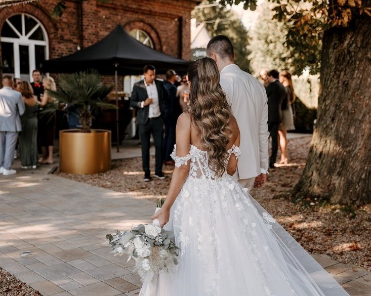 Brautpaar vor der Hochzeitslocation Extrafein-Witten mit Gästen im Gartenbereich