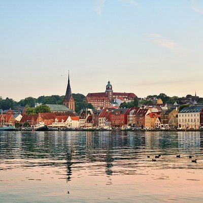 Hochzeit in Flensburg: Malerischer Blick über das ruhige Wasser der Flensburger Förde auf die historische Altstadt bei Sonnenuntergang.