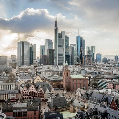 Blick auf die moderne Skyline von Frankfurt am Main mit historischen Dächern im Vordergrund unter leicht bewölktem Himmel.