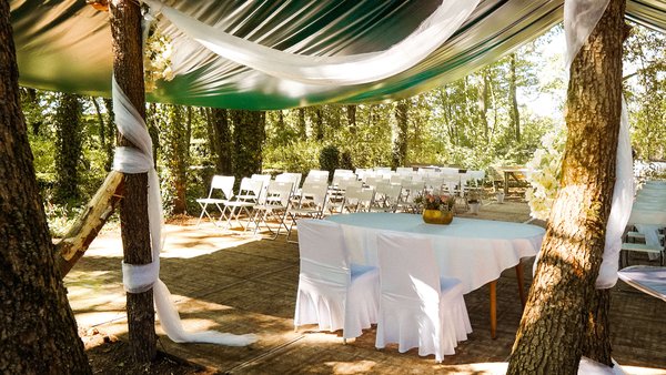 Blick durch den Traubogen auf den gedeckten Tisch und die weißen Stühle für die freie Trauung unter Bäumen nahe Dortmund