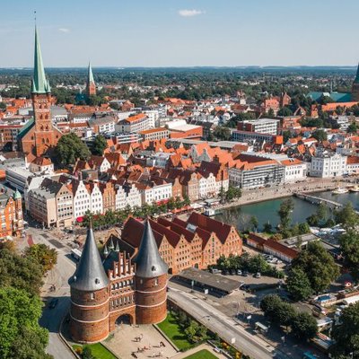 Heiraten in Lübeck: Drohnenaufnahme über das historische Holstentor und die Altstadt an der Trave bei Sonnenschein.