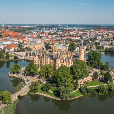 Vogelperspektive auf das prachtvolle Schloss Schwerin auf einer Schlossinsel im Wasser mit der Altstadt im Hintergrund.