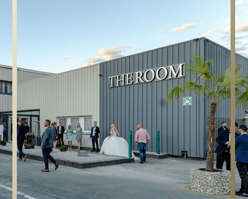 Außenansicht der Hochzeitslocation THE ROOM Bergkamen mit Brautpaar und Gästen vor dem Eingang