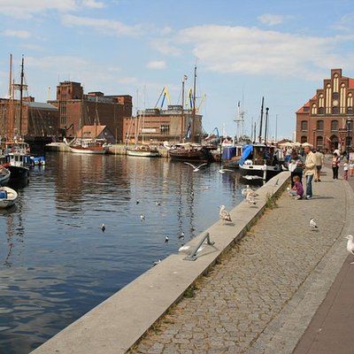 Blick entlang der Uferpromenade am Alten Hafen in Wismar mit historischen Backsteingebäuden und Booten im Wasser.