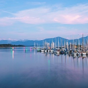 Ein romantischer Yachthafen am Chiemsee bei atmosphärischer Abenddämmerung mit Blick auf die Alpen.