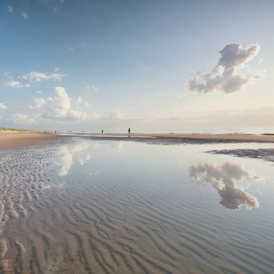 Heiraten an der Nordsee: Weite Wattlandschaft mit Spiegelung im Wasser unter blauem Himmel.