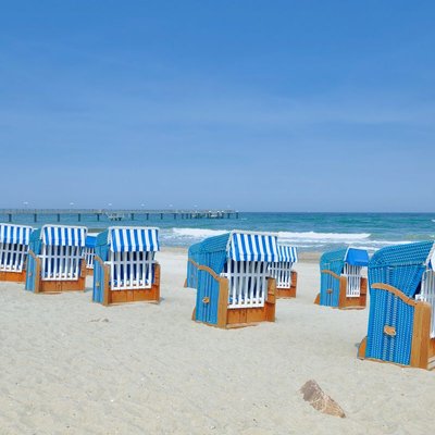 Hochzeit an der Ostsee: Blau-weiße Strandkörbe am feinen Sandstrand mit Blick aufs Meer und eine Seebrücke.