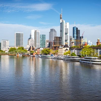 Die beeindruckende Frankfurter Skyline spiegelt sich bei blauem Himmel im Main.