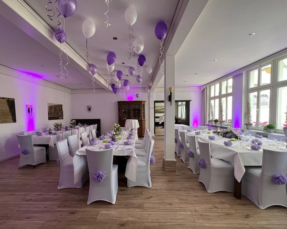 Festlich dekorierter Saal mit lila Ballondeko, weißen Stuhlhussen und violetten Schleifen im Hotel-Restaurant Burbaum in Waltrop