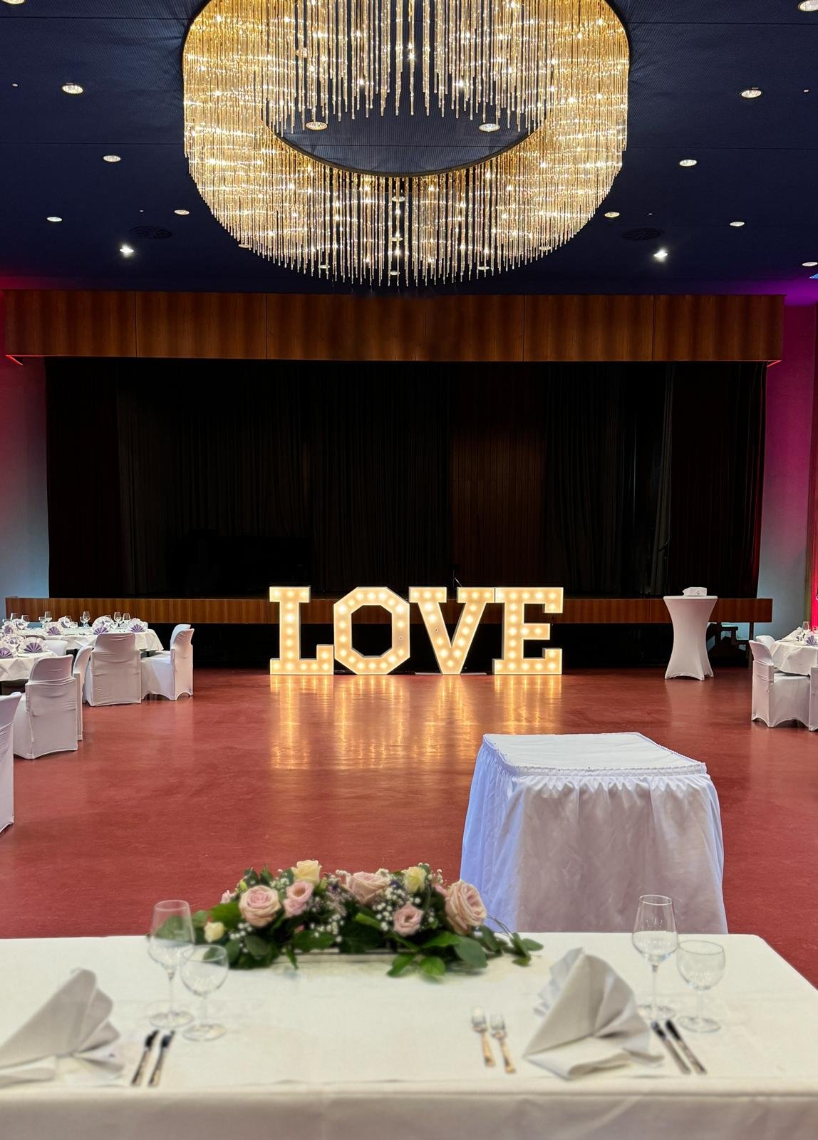 Moderner Hochzeitssaal im Kurhaus Bad Krozingen mit großem Kronleuchter, Bühne und beleuchteten LOVE-Buchstaben als Hochzeitsdekoration.