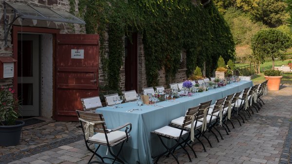 Lange, gedeckte Hochzeitstafel im Außenbereich der Hochzeitslocation Landhaus Bärenmühle