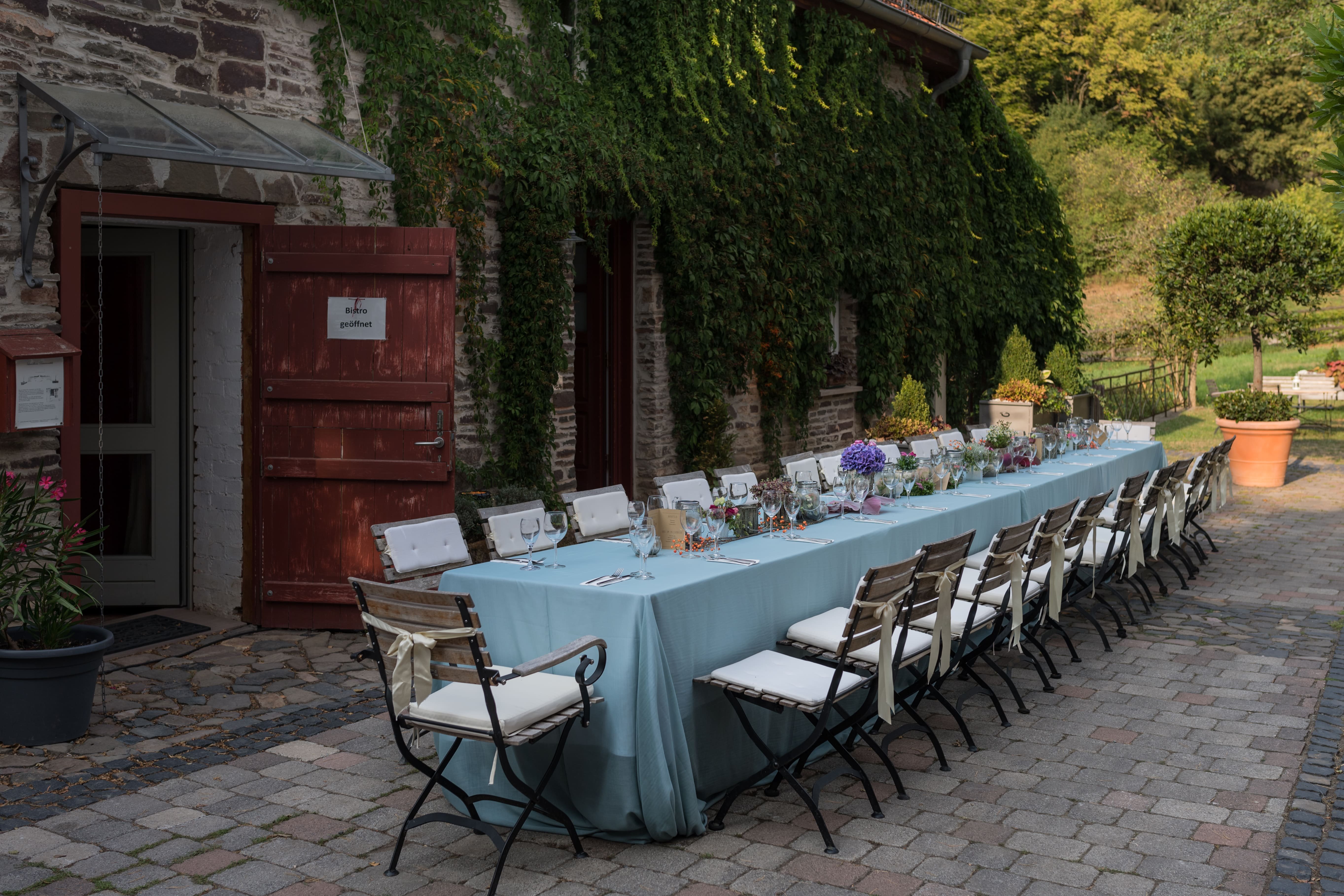 Lange, gedeckte Hochzeitstafel im Außenbereich der Hochzeitslocation Landhaus Bärenmühle