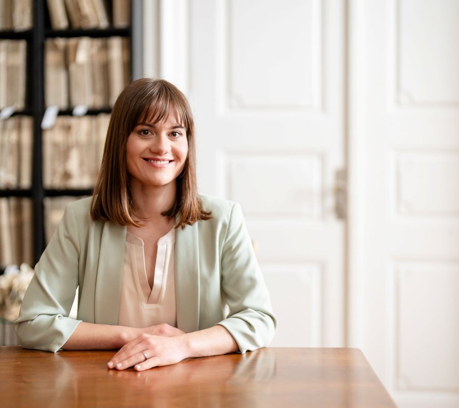 Melanie Chmieliczek, Gründerin von unserehochzeitslocation.de, sitzt lächelnd am Tisch und bietet ein Beratungsgespräch für Hochzeitslocations an.