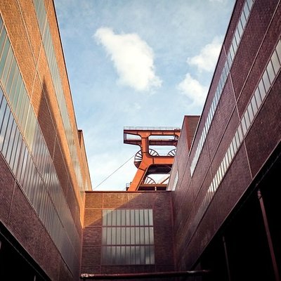 Das rote Fördergerüst der Zeche Zollverein zwischen Backsteingebäuden in Essen